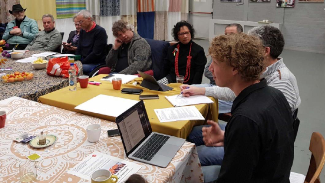 Foto van leden rond een tafel, de bestuursvoorzitter aan het woord.