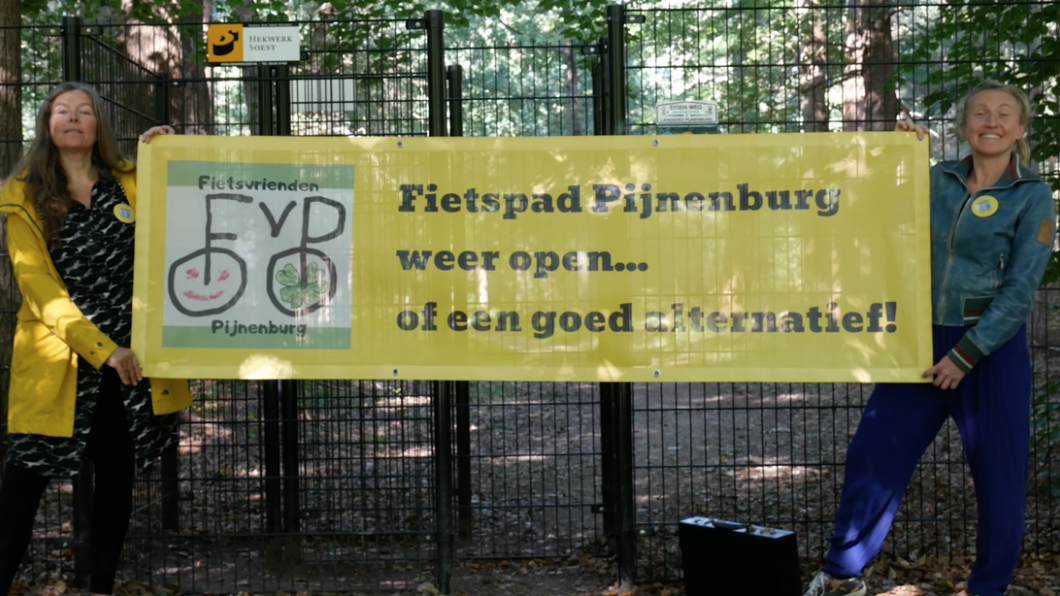 Twee vrouwen met een geel spandoek waarop staat: Fietspad Pijnenburg weer open.. Of een goed alternatief!