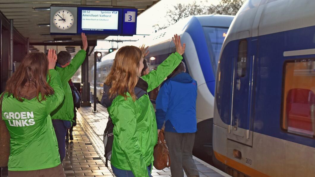 Mensen in GroenLinks-jasje zwaaien passagiers richting de Klimaatmars uit.