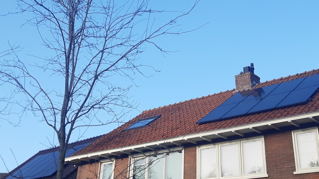 Foto van daken van huizen met zonnepanelen tegen een blauwe lucht.