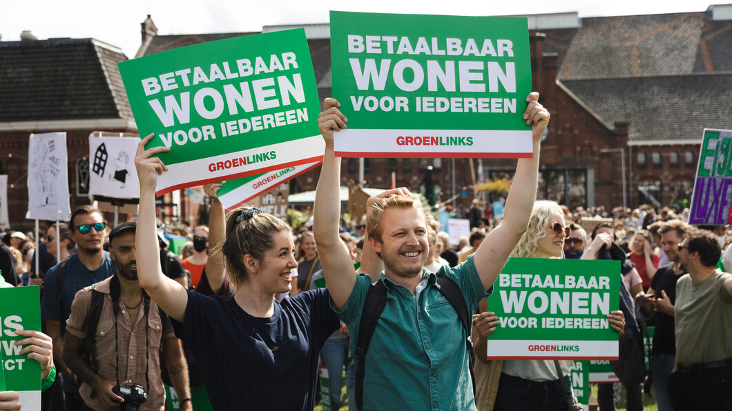 Foto van het woonprotest in Amsterdam. Twee deelnemers houden borden omhoog met de tekst: 'Betaalbaar wonen voor iedereen'.