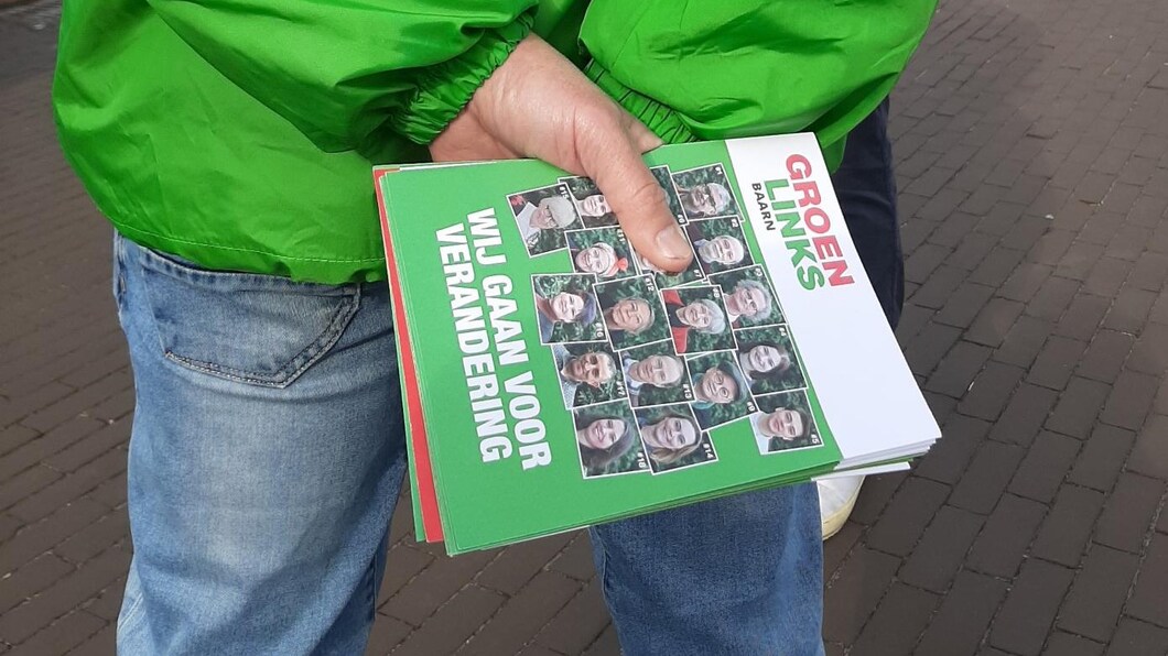 Een vrijwilliger in groen jasje houdt een stapeltje flyers vast met daarop de tekst: Wij gaan voor verandering.