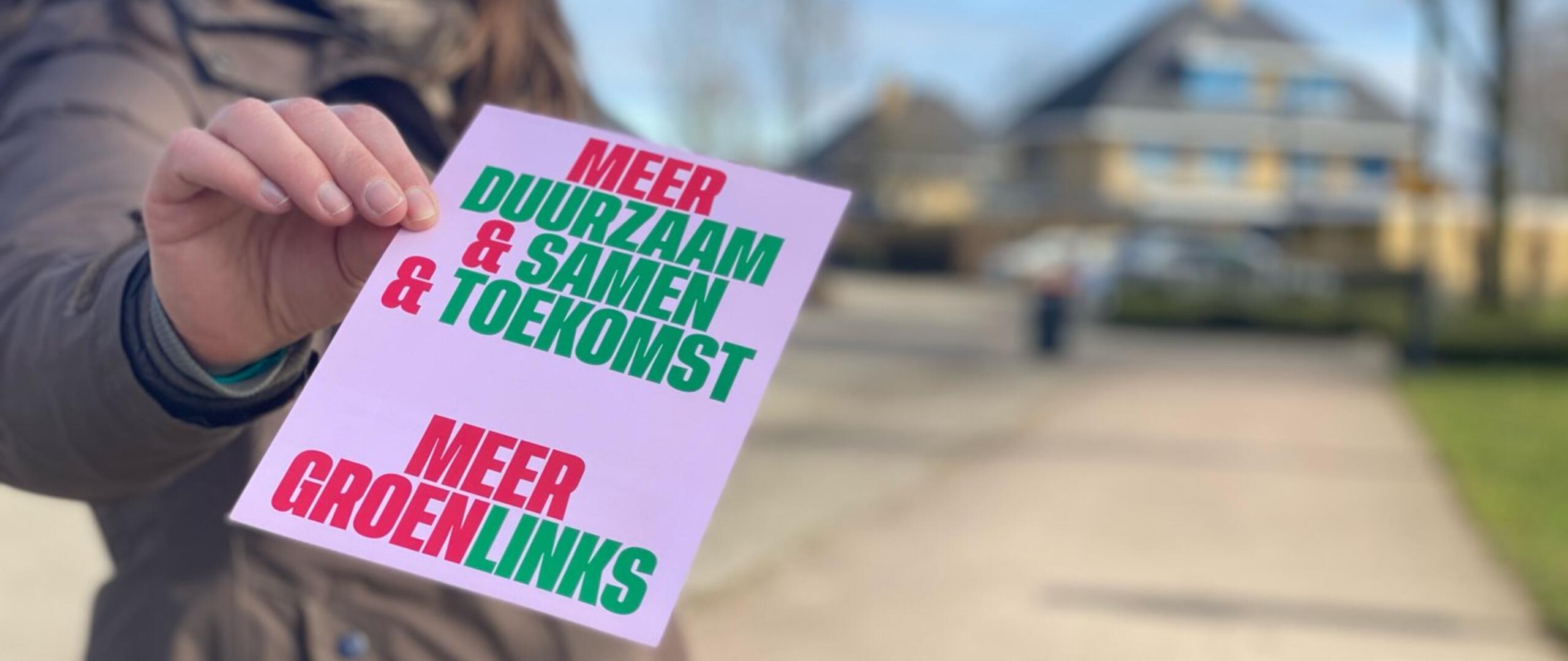 Een vrouw toont een GroenLinks-flyer tegen een vervaagde achtergrond. 