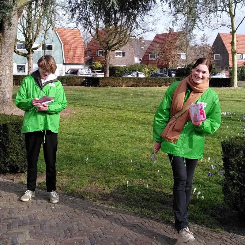Foto van twee vrijwilligers die in een hofje aan het flyeren zijn. 