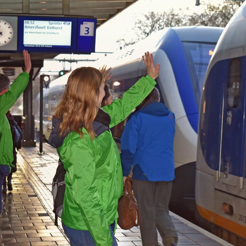 Mensen in GroenLinks-jasje zwaaien passagiers richting de Klimaatmars uit.