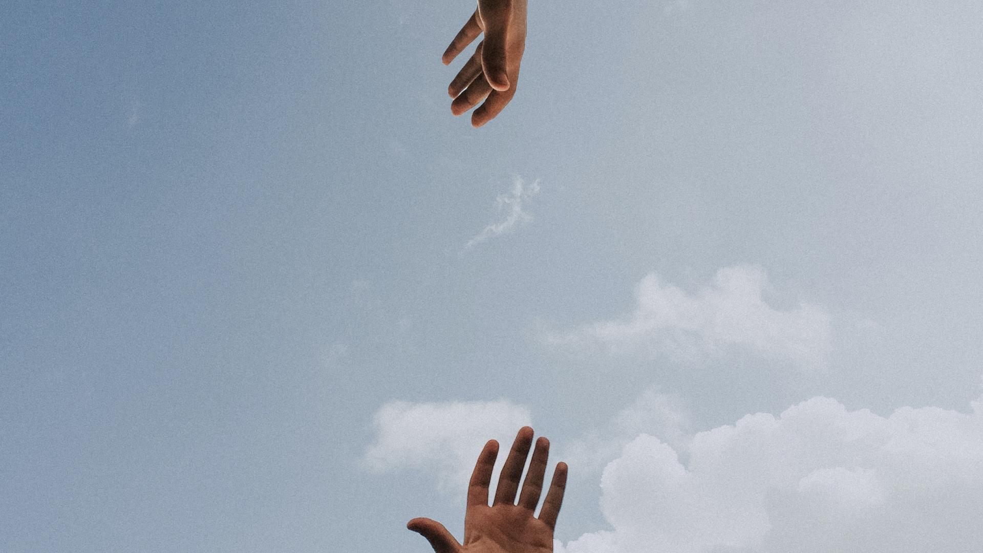 Twee handen die naar elkaar reiken tegen de achtergrond van een blauwe lucht.