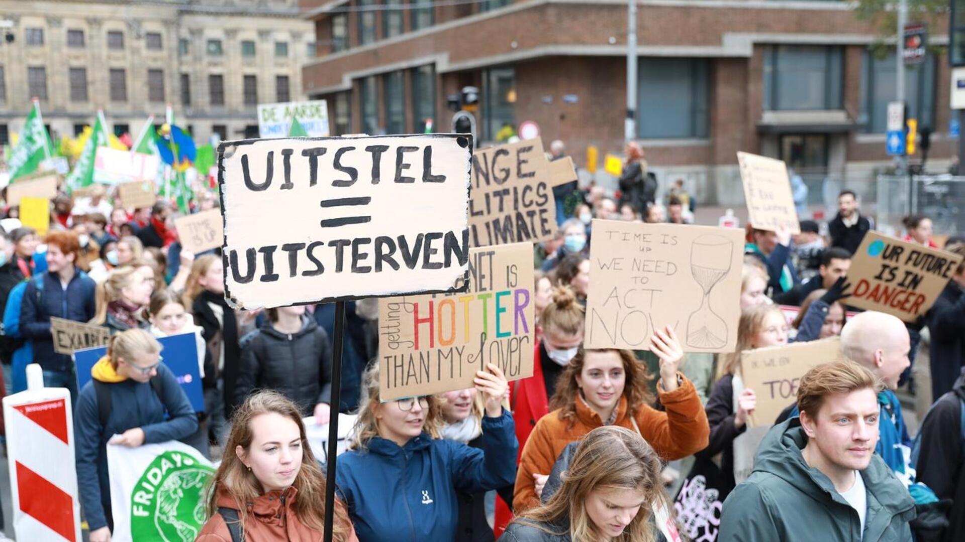 Foto van de Klimaatmars in Amsterdam. In het midden een bord met: Uitstel = uitsterven.