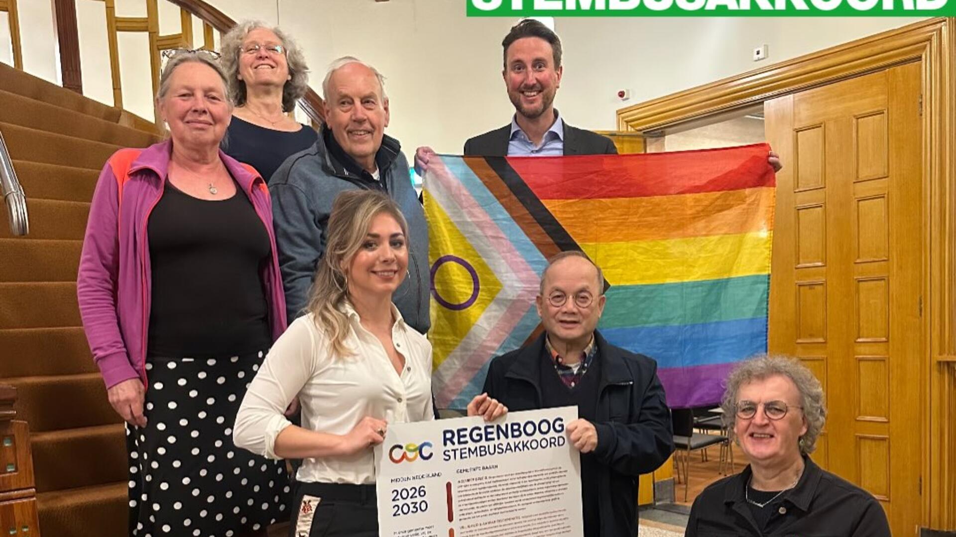 Foto van GroenLinksers op de trap van het gemeentehuis met het Stembusakkoord en een regenboogvlag.